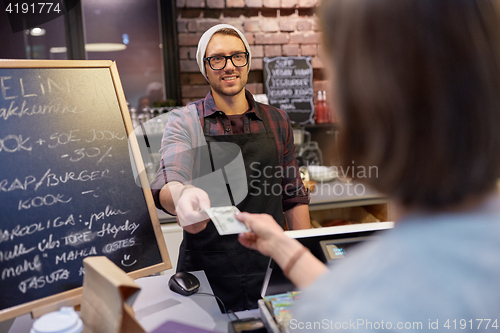 Image of happy barman and woman paying money at cafe