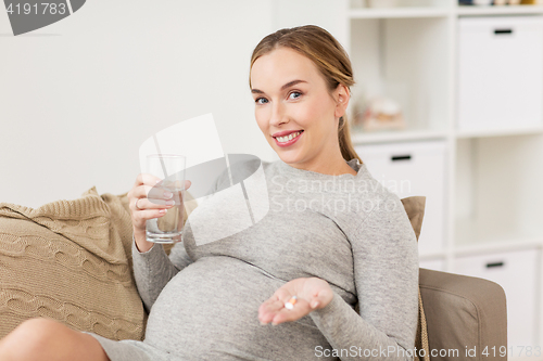 Image of happy pregnant woman with water and pills at home