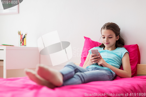 Image of smiling girl texting on smartphone at home