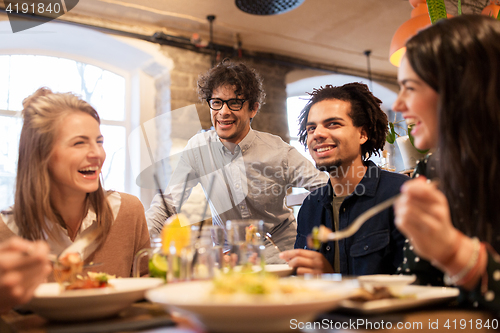 Image of happy friends eating and drinking at restaurant