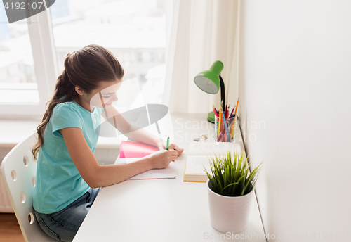 Image of happy girl with book writing to notebook at home