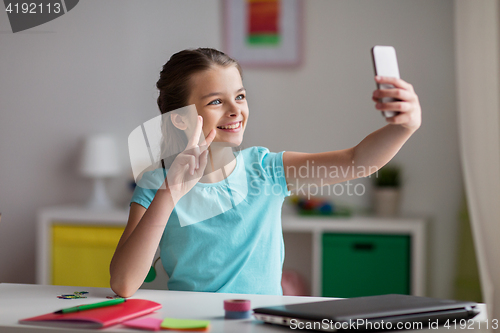Image of happy girl with smartphone taking selfie at home