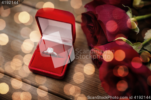 Image of close up of diamond engagement ring and red roses