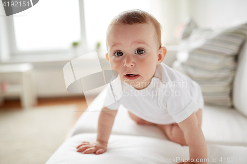 Image of little baby in diaper crawling along sofa at home