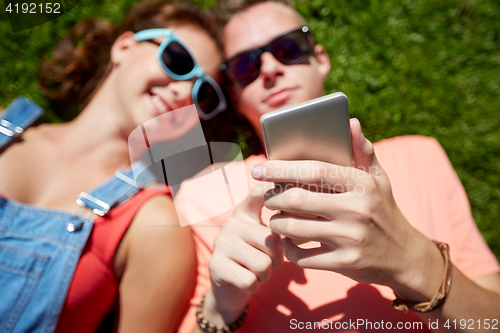 Image of teenage couple with smartphone lying on grass