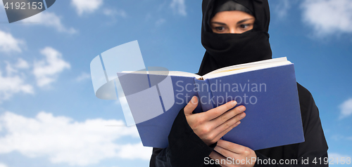 Image of muslim woman in hijab reading book over sky