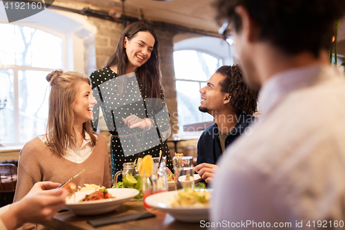 Image of happy friends eating and drinking at restaurant