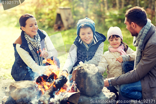 Image of happy family roasting marshmallow over campfire