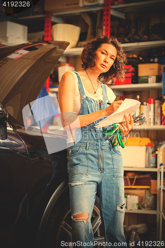 Image of beautiful woman mechanic in blue overalls makes recording