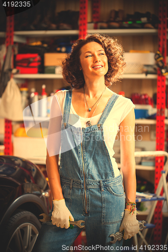 Image of car mechanic smiling woman with wrenches standing near the car