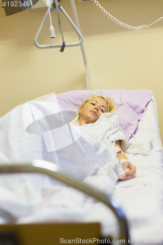 Image of Bedridden female patient recovering after surgery in hospital care.