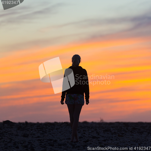 Image of Woman on rocky beach watching sunset.