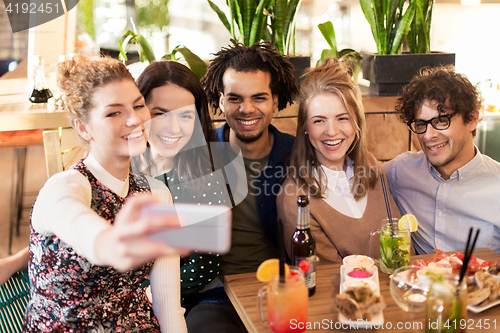 Image of friends taking selfie by smartphone at bar or cafe