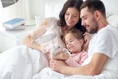 Image of happy child with toy and parents in bed at home