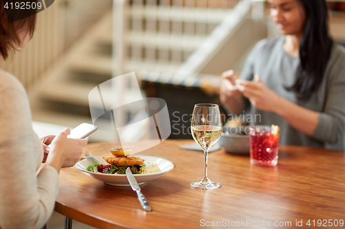 Image of women with smartphones and food at restaurant