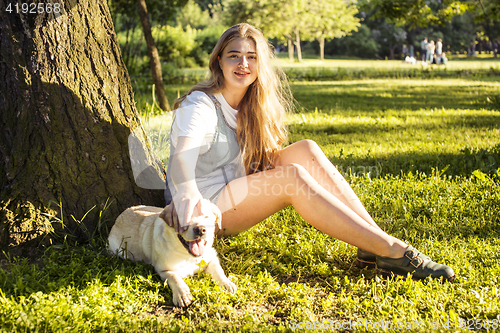 Image of young attractive blond woman playing with her dog in green park at summer, lifestyle people concept