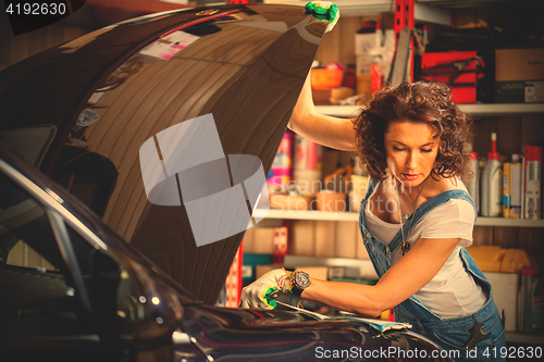 Image of carmechanic in blue overalls reading instruction engine adjustme