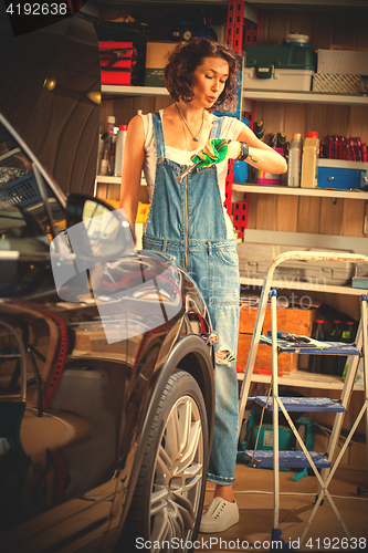 Image of woman mechanic in blue overalls looks at wristwatch