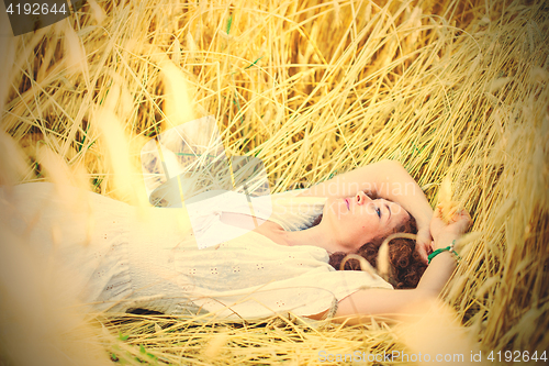 Image of woman in white dress lies in a field among ears of corn