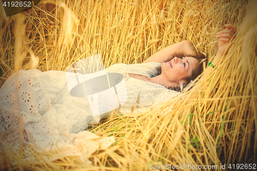 Image of smiling woman in white dress lying among the ears of wheat