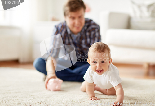 Image of happy father with baby and piggy bank at home