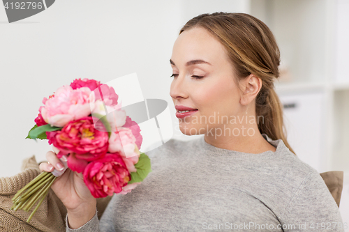 Image of happy woman smelling flowers at home