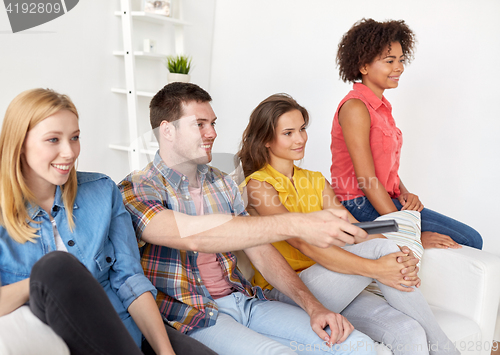 Image of happy friends with remote watching tv at home