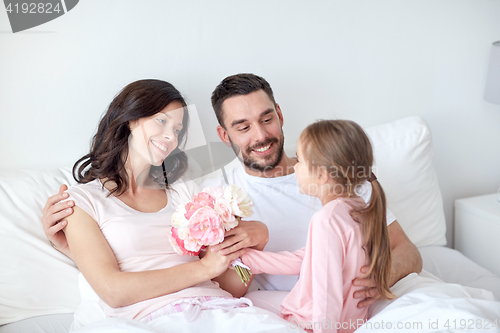 Image of happy girl giving flowers to mother in bed at home