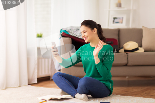 Image of happy woman with smartphone waving hand at home