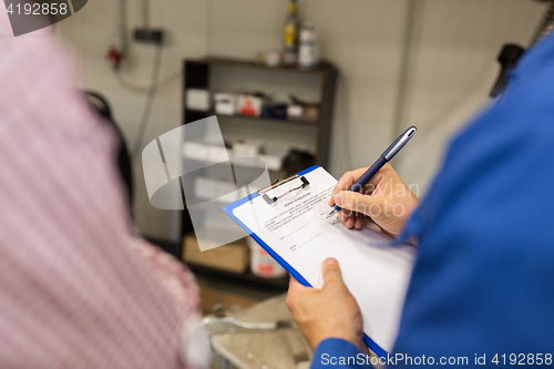 Image of auto mechanic with clipboard and man at car shop