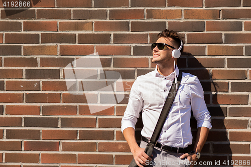 Image of young man in headphones with bag over brickwall