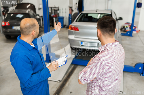 Image of auto mechanic with clipboard and man at car shop