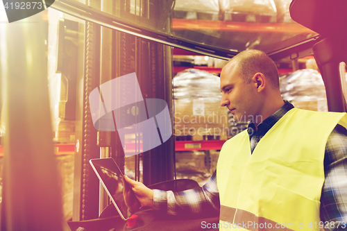 Image of man with tablet pc operating forklift at warehouse