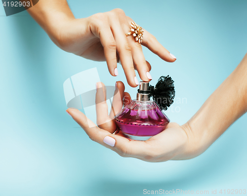 Image of woman hands holding bottle of perfume pink manicure and jewelry on blue background, luxury concept