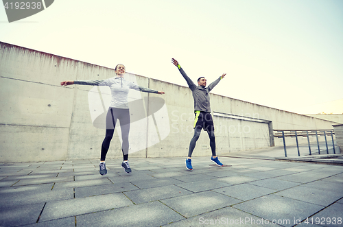 Image of happy man and woman jumping outdoors