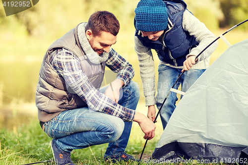 Image of happy father and son setting up tent outdoors