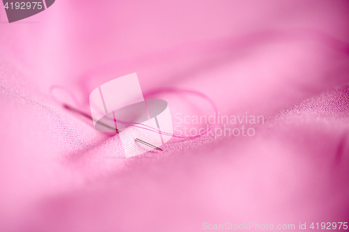 Image of sewing needle with thread stuck into pink fabric