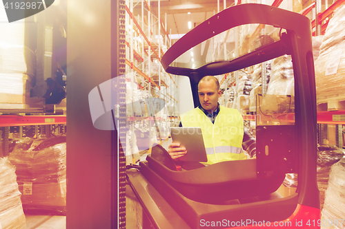 Image of man with tablet pc operating forklift at warehouse