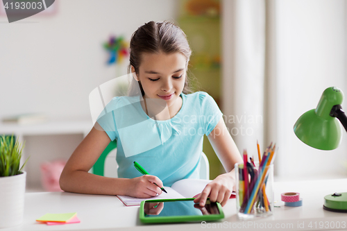 Image of girl with tablet pc writing to notebook at home