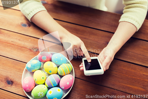 Image of close up of hands with easter eggs and smartphone