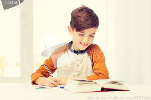 Image of smiling student boy writing to notebook at home