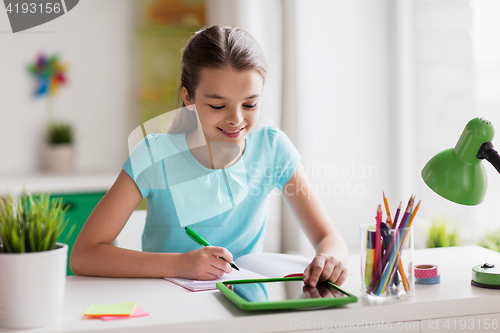 Image of girl with tablet pc writing to notebook at home