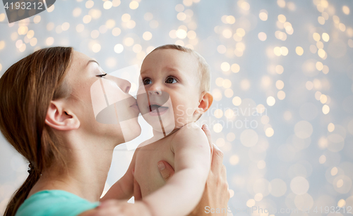 Image of happy young mother kissing little baby over lights