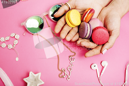 Image of woman hands holding macaroons with lot of girl stuff on pink background, girls accessories concept