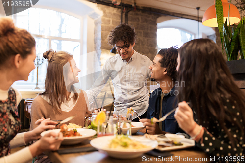 Image of happy friends eating and drinking at restaurant