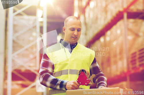 Image of man in safety vest packing box at warehouse