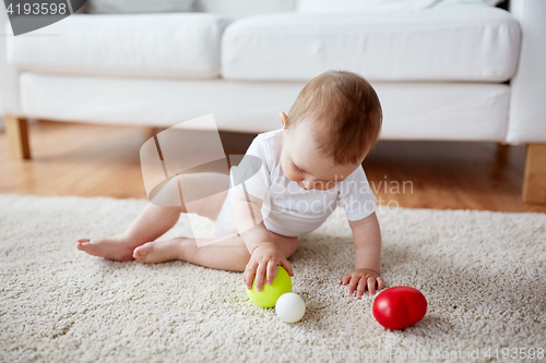 Image of happy baby playing with balls on floor at home