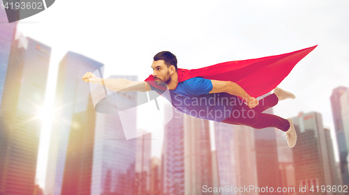 Image of man in red superhero cape flying over city