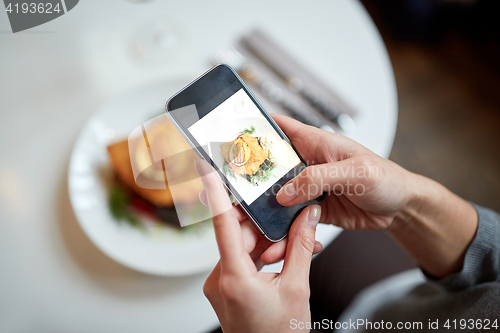 Image of woman with smartphone photographing food at cafe