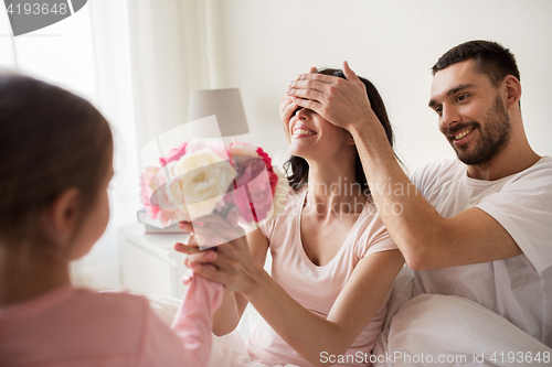 Image of happy girl giving flowers to mother in bed at home